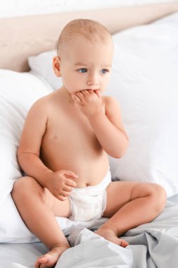 Yumuşak beyaz yastıklar ile yatakta oturan sevimli küçük çocuk