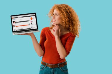 Kiev, Ukrayna - 16 Temmuz 2019: soundcloud web sitesi ile dizüstü bilgisayar tutan dalgın kızıl saçlı kadın, mavi izole 