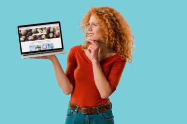 Kiev, Ukrayna - 16 Temmuz 2019: mevduat fotoğrafları web sitesi ile dizüstü bilgisayar tutan dalgın kızıl saçlı kadın, mavi izole 