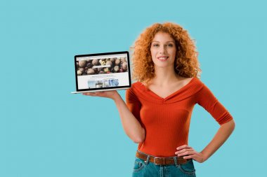 Kiev, Ukrayna - 16 Temmuz 2019: depositphotos web sitesi ile dizüstü bilgisayar tutan gülümseyen kızıl saçlı kadın, mavi izole 
