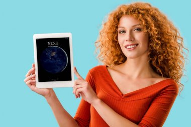 Kiev, Ukrayna - 16 Temmuz 2019: ipad ile dijital tablet tutan gülümseyen kızıl saçlı kadın, mavi izole 