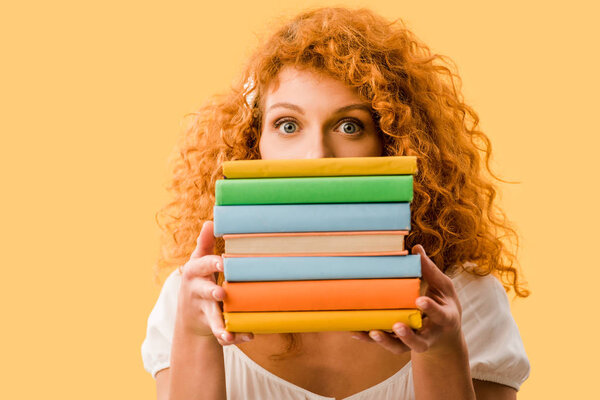 female redhead student holding books isolated on yellow 