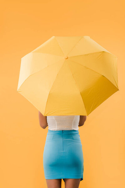 back view of woman standing with umbrella isolated on yellow