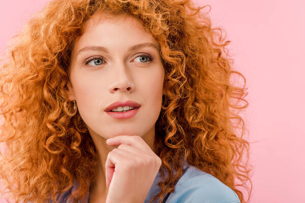 attractive pensive redhead woman isolated on pink