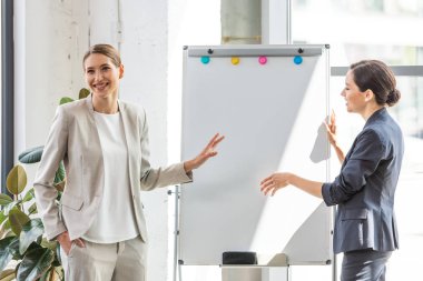 ofiste flipchart yakınında duran resmi giyim iki gülümseyen iş kadını