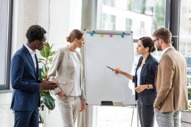 ofiste flipchart yakınında duran resmi giyim dört çok ırklı meslektaşları