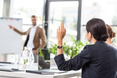 back view of businesswoman raising hand during conference in office