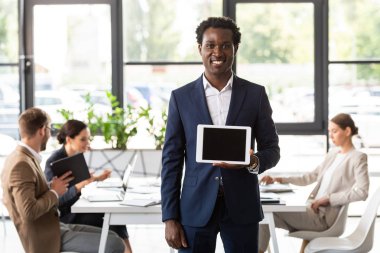 ofiste boş ekran ile dijital tablet tutan resmi giyim gülümseyen Afrikalı Amerikalı işadamı nın ön görünümü