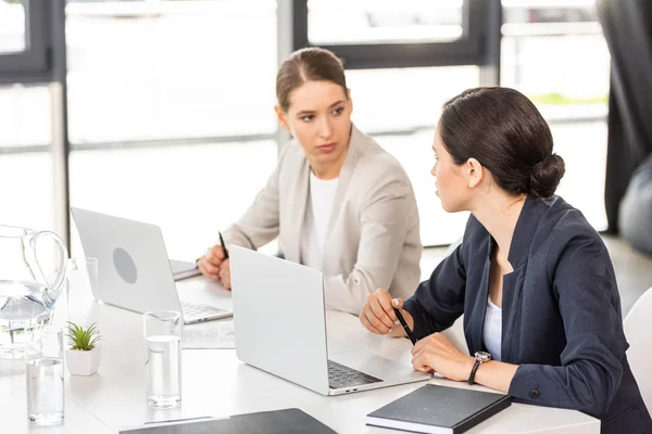 Duas Mulheres Negócios Sentadas Mesa Com Laptops Olhando Umas Para — Fotografia de Stock