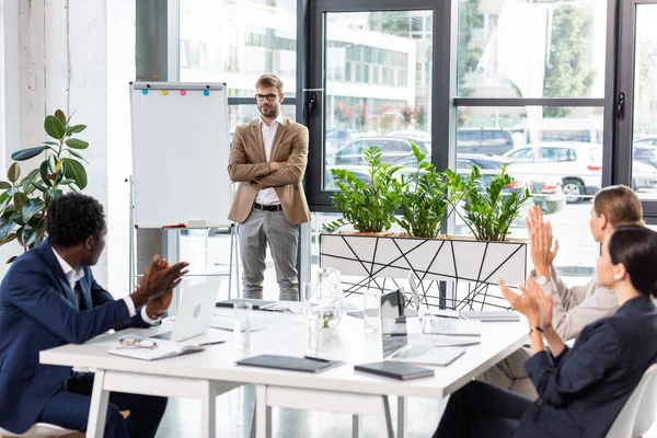 Uśmiechnięty Biznesmen Okularach Stojących Skrzyżowanymi Ramionami Pobliżu Flipchart Podczas Konferencji — Zdjęcie stockowe