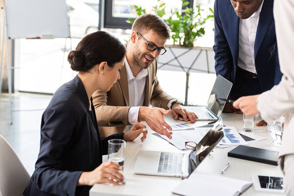 partial view of multiethnic businesspeople at table during conference in office