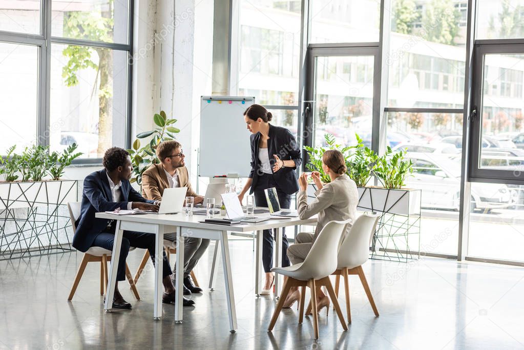 multiethnic businesspeople at table with laptops during conference in office