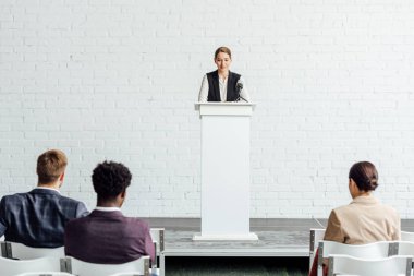 attractive businesswoman standing and talking during conference in conference hall clipart