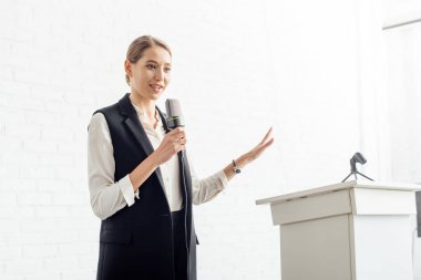 konferans salonunda konferans sırasında mikrofon tutan ve konuşan çekici iş kadını