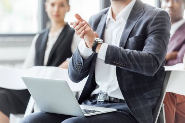 konferans sırasında dizüstü bilgisayar tutan ve alkışlayan resmi giyim işadamının kırpılmış görünümü 
