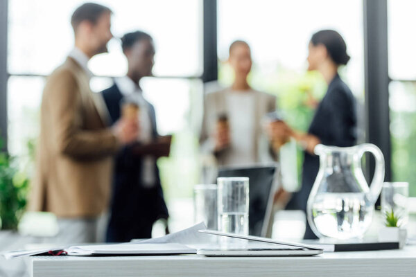 selective focus of four multiethnic colleagues holding disposable cups of coffee and smiling in office