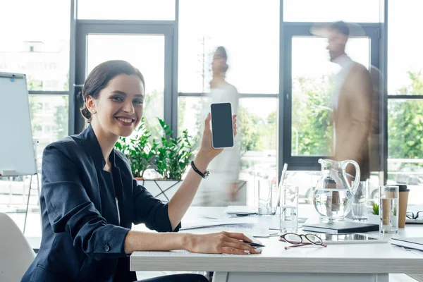 smiling and attractive businesswoman in formal wear holding smartphone