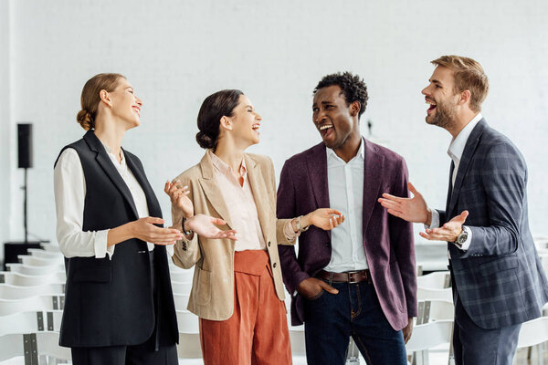 four multiethnic colleagues in formal wear talking in conference hall