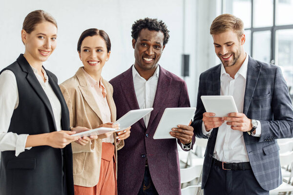 четверо мультиэтнических коллег держат цифровые планшеты и разговаривают в конференц-зале
