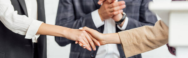 panoramic shot of colleagues in formal wear shaking hands in conference hall 