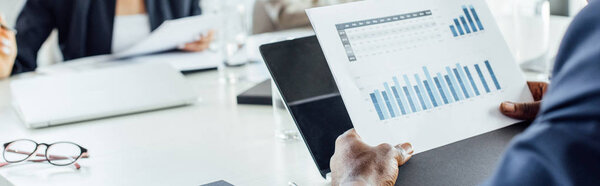 панорамный снимок африканского американского бизнесмена, держащего документ с графиками в офисе
 