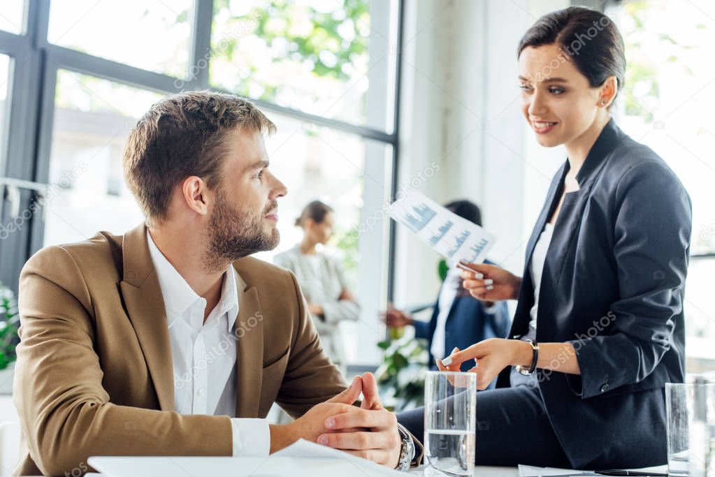 attractive businesswoman sitting on table and talking to colleague