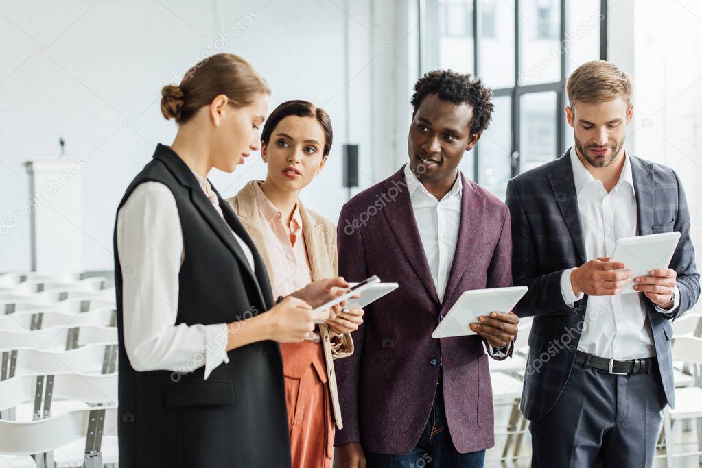 four multiethnic colleagues holding digital tablets and talking in conference hall