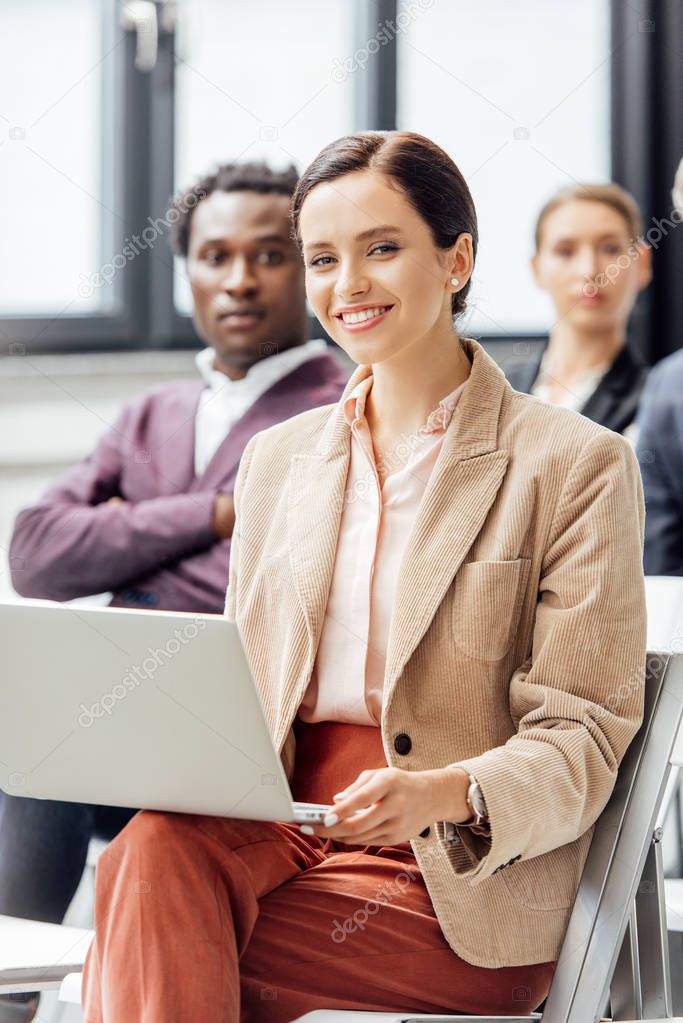 selective focus of attractive woman in formal wear holding laptop during conference 