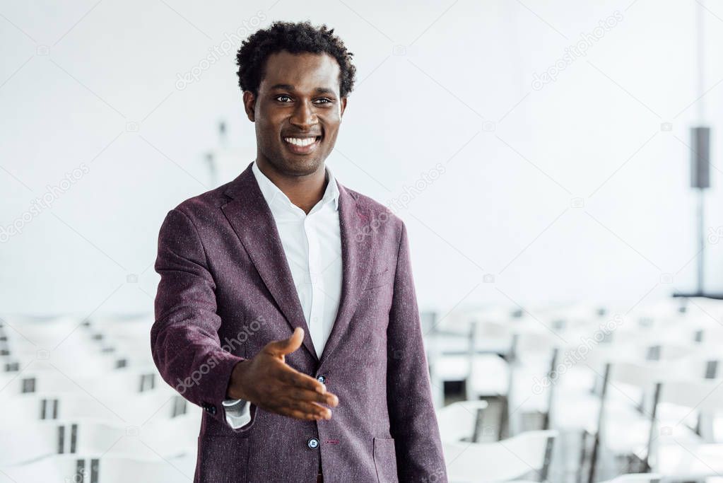 african american businessman in formal wear with outstretched hand smiling in conference hall