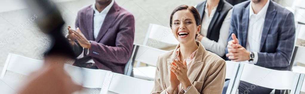 panoramic shot of attractive businesswoman smiling and clapping during conference 