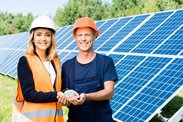handsome engineer and businesswoman smiling and holding solar energy battery model 