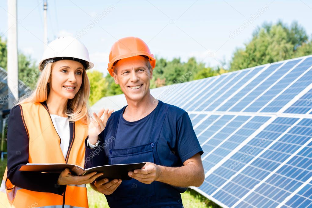 handsome engineer and businesswoman smiling and holding folder 