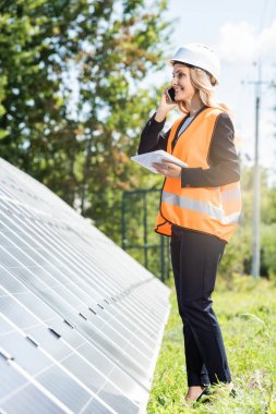 güvenlik yelek ve hardhat akıllı telefon konuşuyor ve dijital tablet tutan iş kadını 