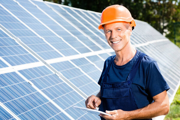 handsome engineer in t-shirt and orange hardhat smiling and holding digital tablet 