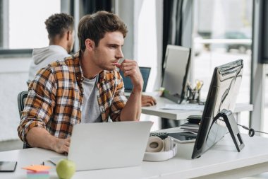 selective focus of serious programmer working near african american colleague in office clipart