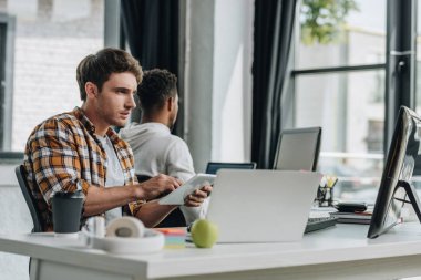 selective focus of young programmer working in office near african american colleague clipart