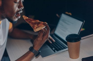 genç afrikalı amerikalı programcı işyerinde otururken pizza yeme