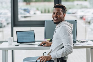 ofiste işyerinde otururken kameraya gülümseyen neşeli afrikalı-amerikalı programcı
