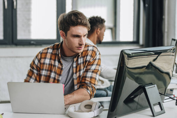 selective focus of thoughtful programmer working near african american colleague in office