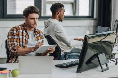 afro-Amerikan meslektaşının yanında otururken dijital tablet kullanarak genç programcı