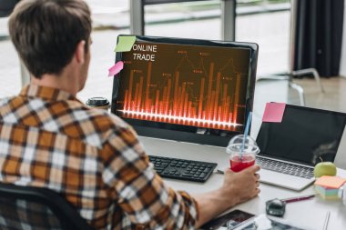 ekranda online ticaret ile bilgisayar monitörü yakınında işyerinde otururken meyve suyu cam tutan genç programcı nın geri görünümü