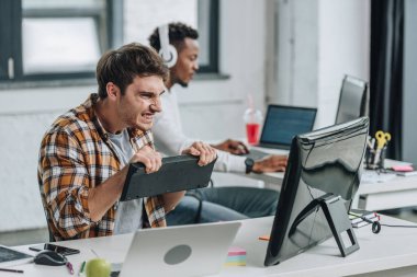 ofiste Afro-Amerikan meslektaşının yanında otururken klavye tutan ve bilgisayar monitörü bakarak kızgın programcı seçici odak