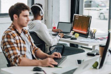 ofiste meslektaşıyakın monitörde online ticaret ile bilgisayar kullanarak Afrikalı-Amerikalı programcı geri görünümü