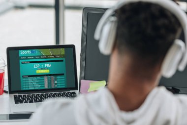 Kiev, Ukrayna - 29 Temmuz 2019: ekranda Sportsbet web sitesi ile dizüstü bilgisayar yakınında oturan kulaklık afro-amerikan programcı geri görünümü