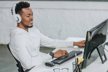 mutlu afrikalı amerikalı programcı kulaklık işyerinde oturan