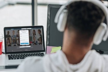 Kiev, Ukrayna - 29 Temmuz 2019: ekranda Linkedin web sitesi ile dizüstü bilgisayar yakınında oturan kulaklık afro-amerikan programcı geri görünümü