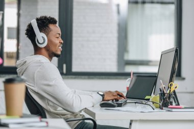 ofiste işyerinde oturan kulaklıklar içinde gülümseyen afro-amerikan programcı