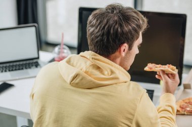 ofiste işyerinde otururken pizza yiyen genç programcının geri görünümü