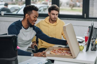 ofiste meslektaşının yanında otururken pizza kutusu açılış gülümseyen afrikalı Amerikalı programcı