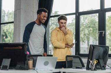 ofiste düşünceli meslektaşın yanında duran gülümseyen afrikalı-Amerikalı programcı